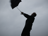 black and white image of a man struggling to hold an umbrella high in the air in high winds