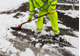A worker in high visibility protective clothing uses a shovel to move heavy snow from the road